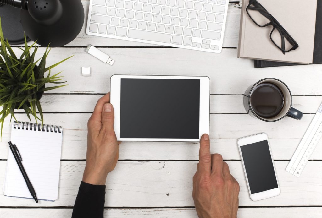 Top view office desk with tablet and smartphone for responsive web or mobile application design. Man pointing to screen.