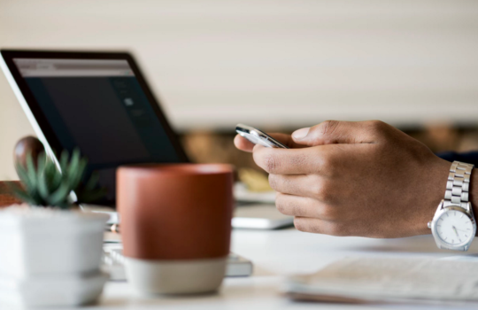 A person using their phone while their laptop is open in the background.