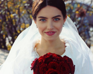 A frontal portrait of a smiling bride holding a bouquet.