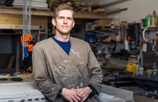 A man leaning against a workbench in his workshop.