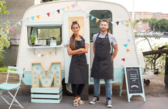 Two business owners stood in front of a converted caravan.