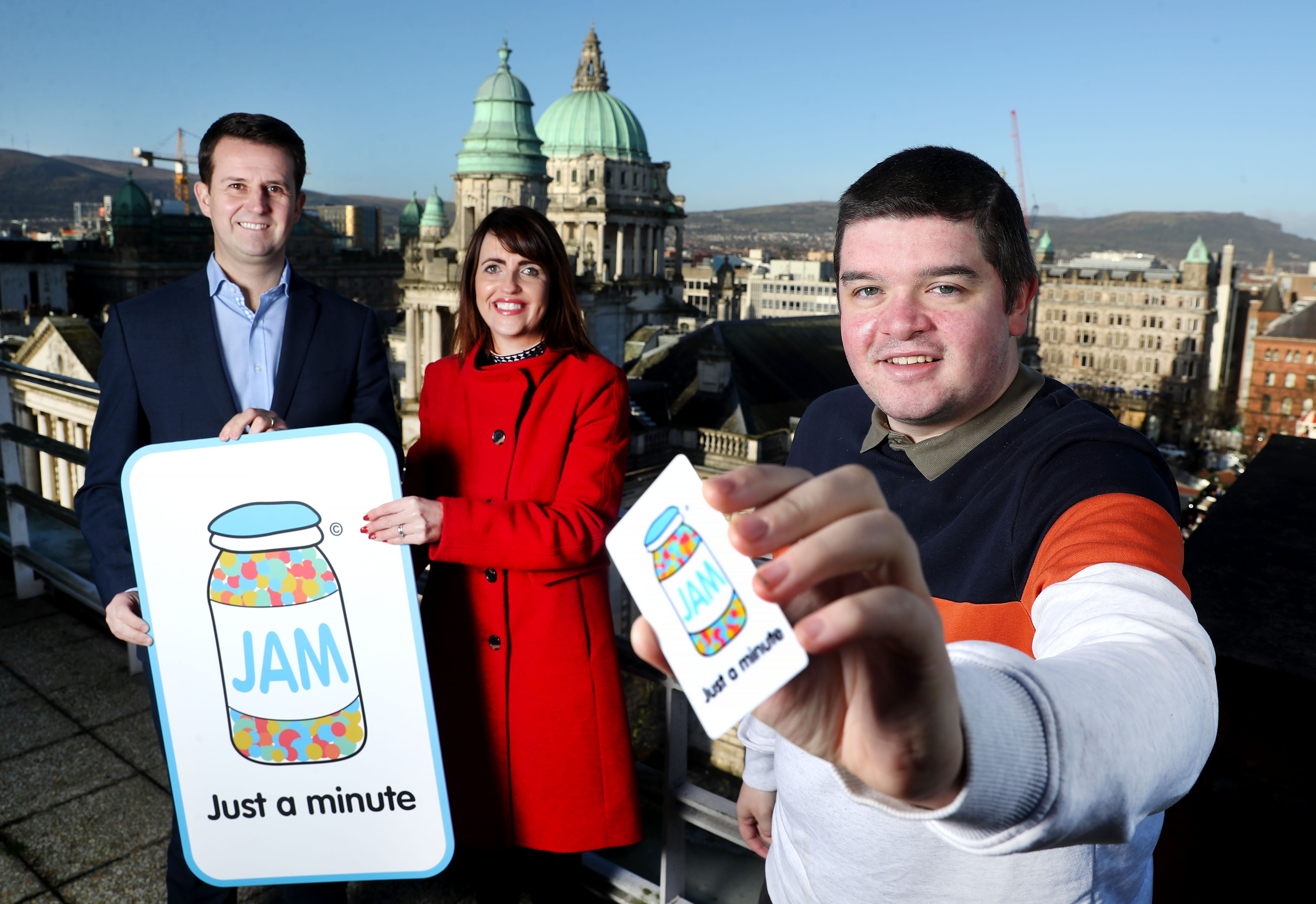 Three people on a rooftop showing their Just A Minute, or JAM, cards.