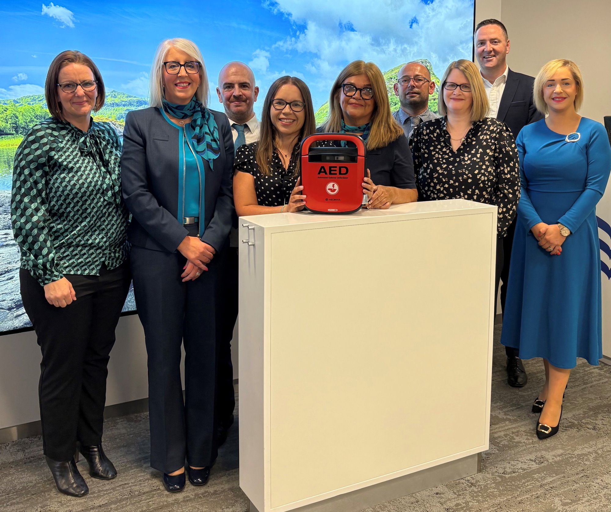 Colleagues from Bank of Ireland in the Coleraine branch holding a defibrillator which has been installed to the side of the branch for community use.