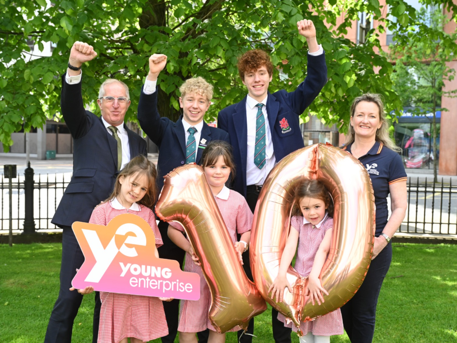 George Higginson and Carol Fitzsimons with a few young people smiling and cheering while holding Young Enterprise Northern Ireland logo and balloons depicting number ten